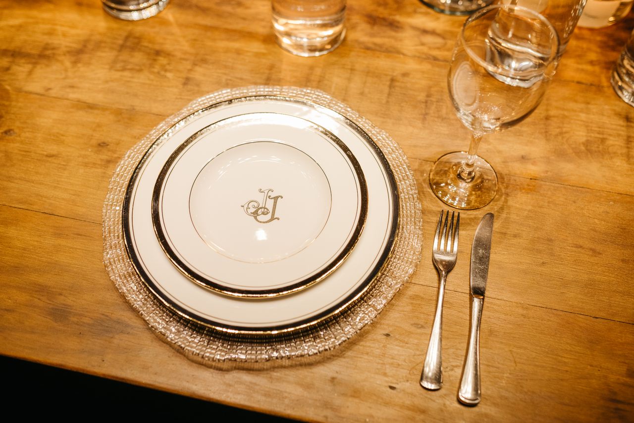 journey-01 Luxurious dinner setting with monogrammed plates, cutlery, and glassware on a wooden table.